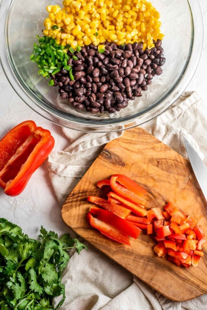 Chopped bell pepper on a cutting board beside a bowl of black beans, corn and jalapeno.