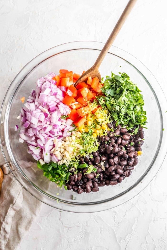 Black beans, red onion, lime zest, garlic, bell pepper, corn and jalapeno in a glass mixing bowl.