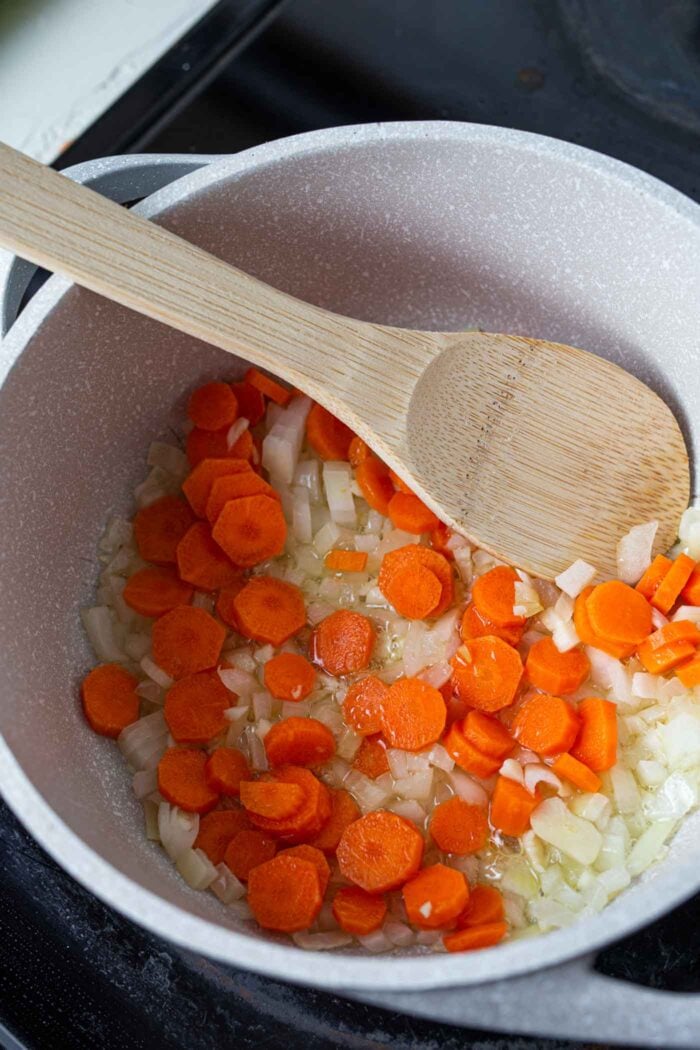 Onions, carrots and garlic simmering in a soup pot with a wooden spoon.