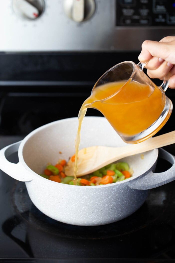 A hand pouring vegetable stock into a soup pot.