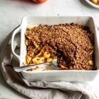 Grain-free vegan apple crisp being scooped out of a white baking dish.