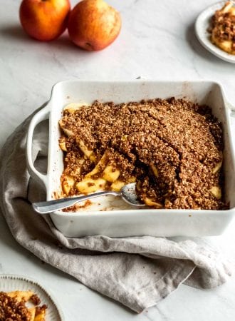 Grain-free vegan apple crisp being scooped out of a white baking dish.