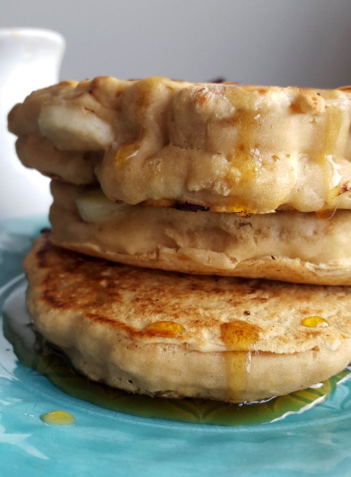 Stack of 3 thick banana pancakes drizzled with maple syrup on a plate.