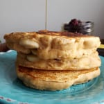 Drizzling maple syrup onto a stack of pancakes on a plate.