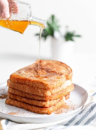 A stack of coconut vegan french toast being topped with maple syrup.
