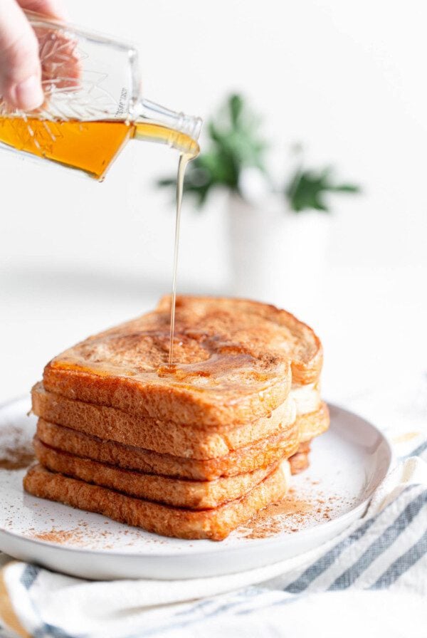 A stack of coconut vegan french toast being topped with maple syrup.