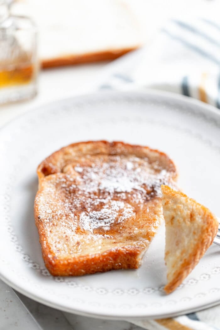 A slice of vegan French toast toped with sugar and maple syrup on a white plate.