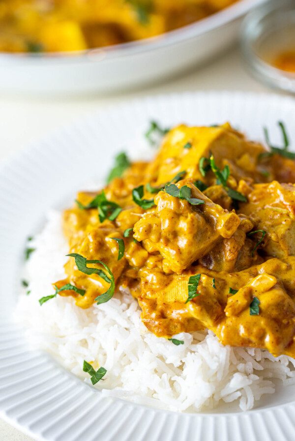 Vegan butter chicken made with tofu on top of white rice and sprinkled with cilantro on a plate.