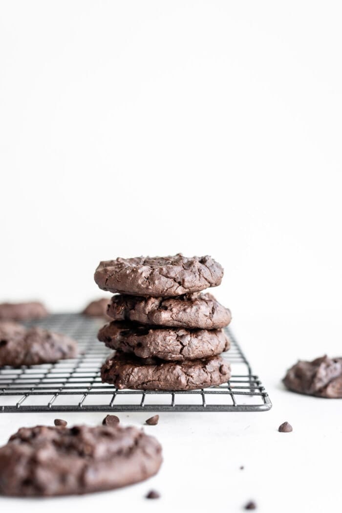 Stack of 4 chocolate vegan protein cookies sitting on a cooling rack with some chocolate chips sprinkled around them.