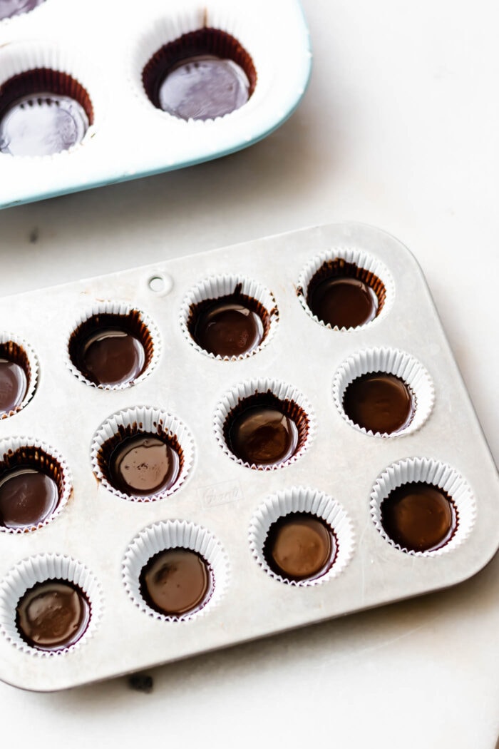 A mini muffin tin with muffin liners filled half-way with liquid vegan chocolate.