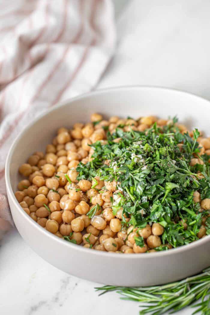 Chopped fresh rosemary and parsley in a bowl with chickpeas.