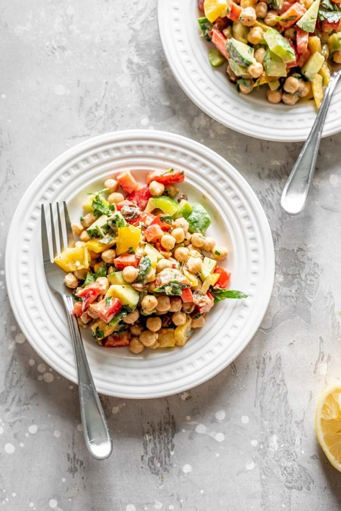 Two white plates with a chickpea bell pepper salad with tahini dressing on them.