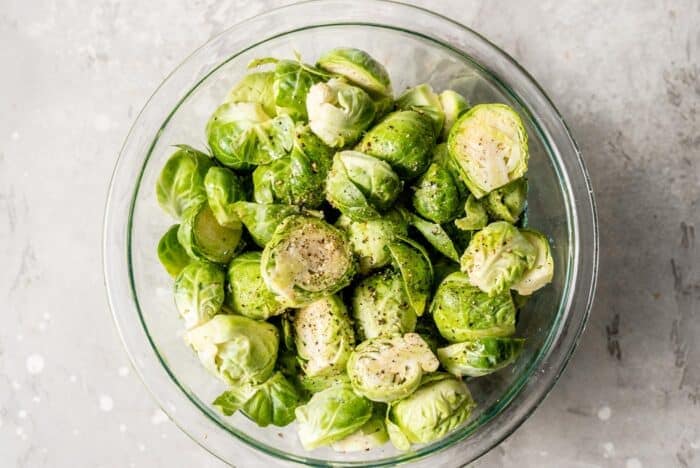Chopped brussels sprouts in a mixing bowl with olive oil, salt and pepper.