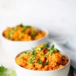 Two white bowls of vegan red lentil cauliflower curry topped with cilantro.