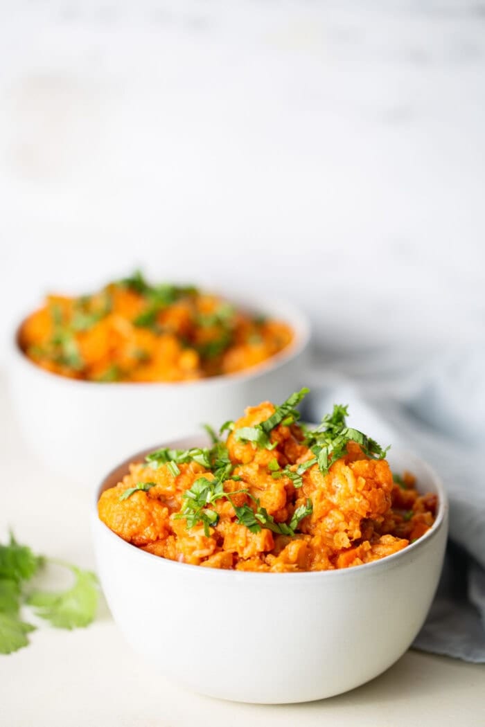 Two white bowls of vegan red lentil cauliflower curry topped with cilantro.