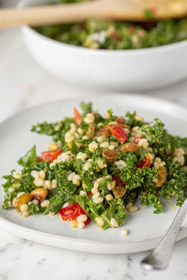 A plate of kale salad with bell peppers, pistachios and barley.