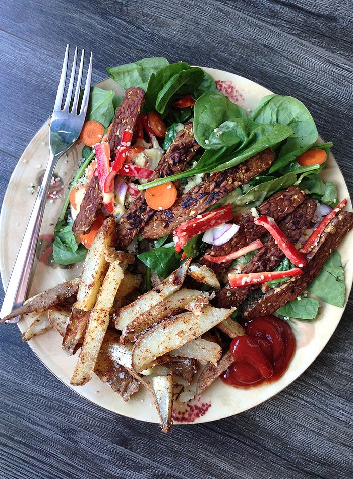 A big plate of green salad with tempeh and baked potato wedges.