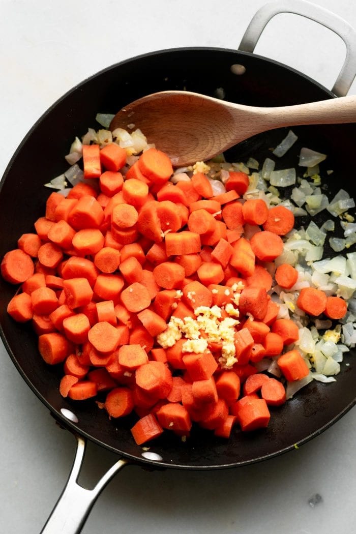 Cooking carrots, ginger, onion and garlic in a sauce pan to make coconut ginger carrot soup.