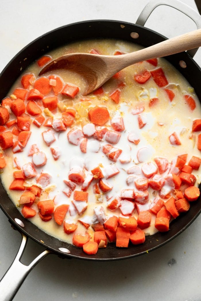 Carrots and coconut milk in a skillet with a wooden spoon.