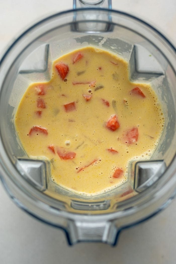 Creamy soup in a blender with carrot chunks in it.