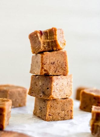 Stack of 4 pieces of pumpkin fudge on a square of parchment paper with a few more pieces of fudge scattered around.