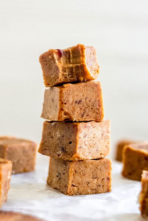 Stack of 4 pieces of pumpkin fudge on a square of parchment paper with a few more pieces of fudge scattered around.