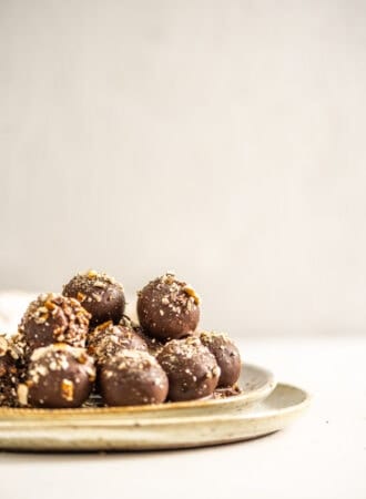 A plate full of chocolate covered truffles topped with crushed pretzels.