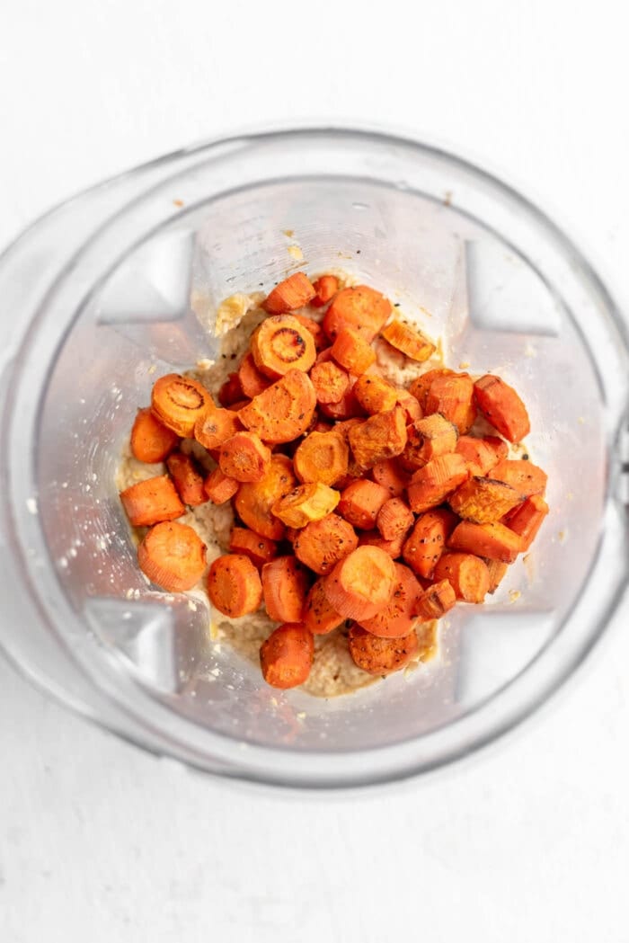 Roasted carrots in a blender container with hummus.