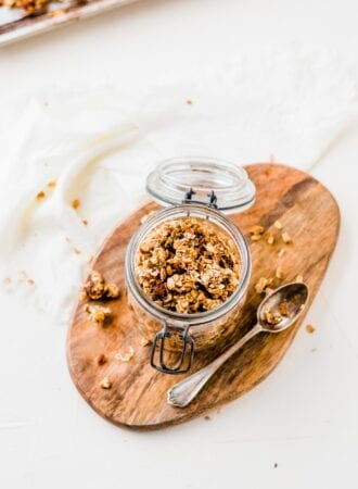 Open jar of pumpkin spice latte granola sitting on a cutting board with a spoon beside it.