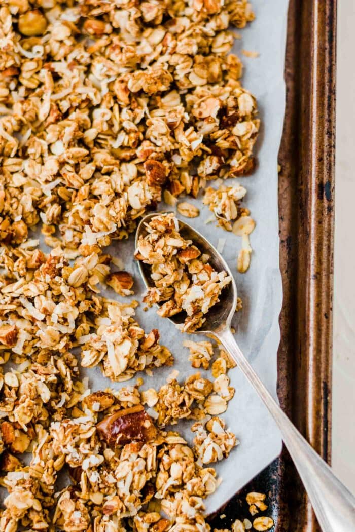Baked granola on a baking tray with a spoon.