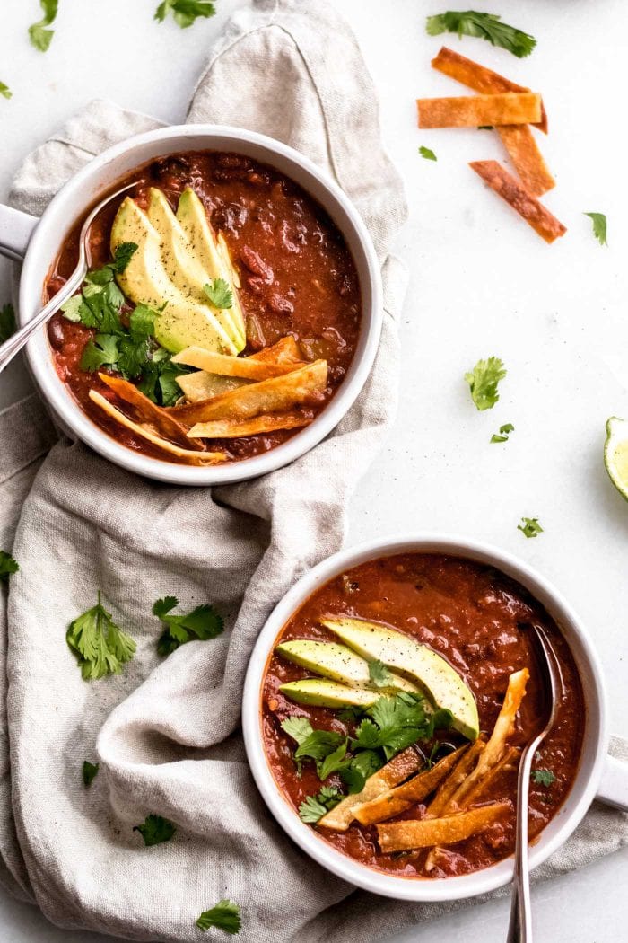 The Best Vegan Tortilla Soup in two bowls topped with avocado, cilantro and tortillas.