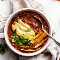 Bowl of tortilla soup topped with avocado, cilantro and tortilla strips.