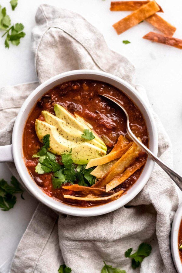 Bowl of tortilla soup topped with avocado, cilantro and tortilla strips.