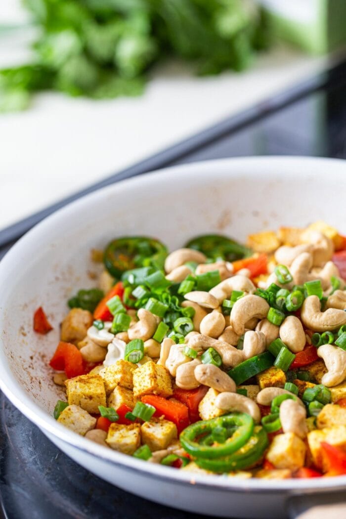 A skillet of cashews, tofu and veggies cooking on a stovetop.