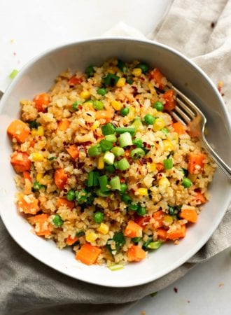 Bowl of cauliflower fried rice with green onion, carrot, peas and corn.
