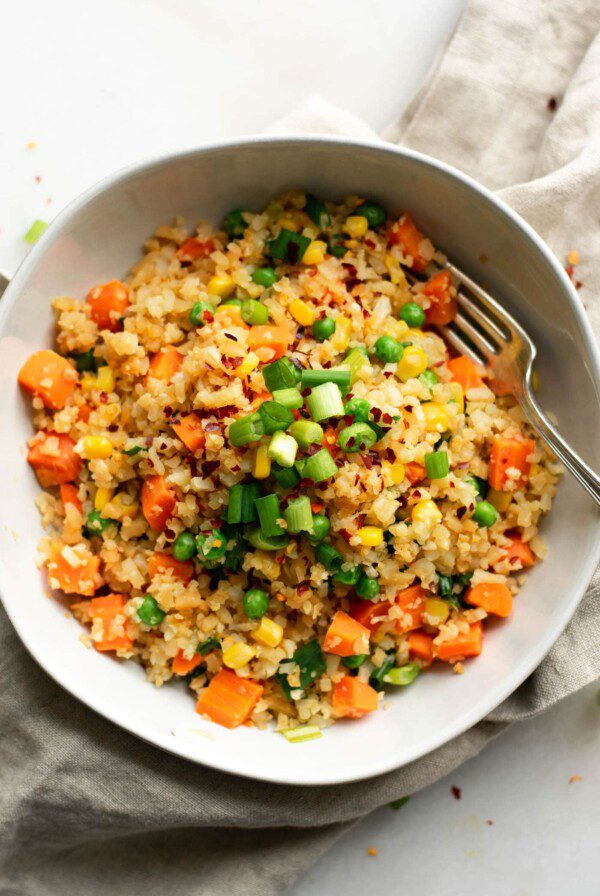 Bowl of cauliflower fried rice with green onion, carrot, peas and corn.