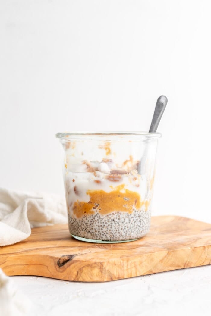 Mashed sweet potato, yogurt, pecans and chia pudding in a jar against a white background.