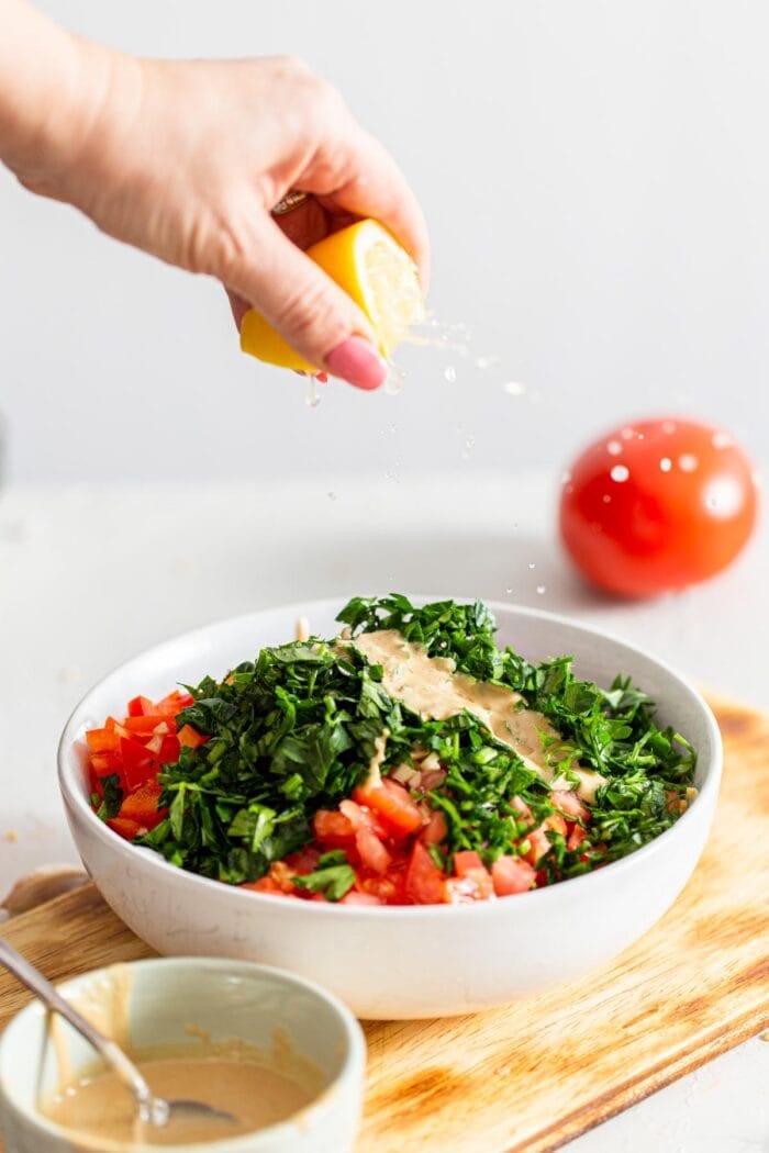 Squeezing lemon into a bowl of parsley and bell pepper.