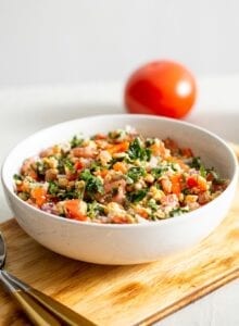 A bowl of tabouleh salad with a tomato in the background.