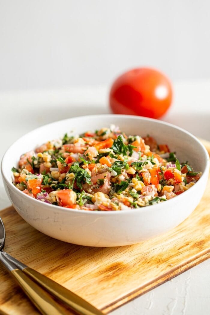 A bowl of tabouleh salad with a tomato in the background.