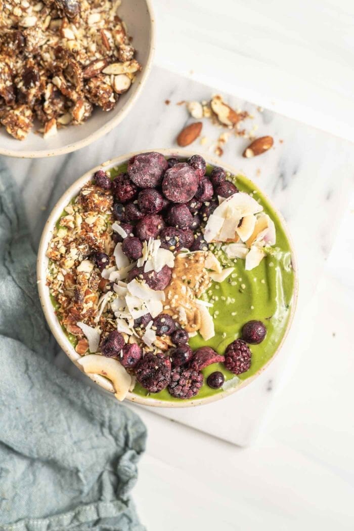 A thick green smoothie in a bowl topped with berries, coconut and nuts.