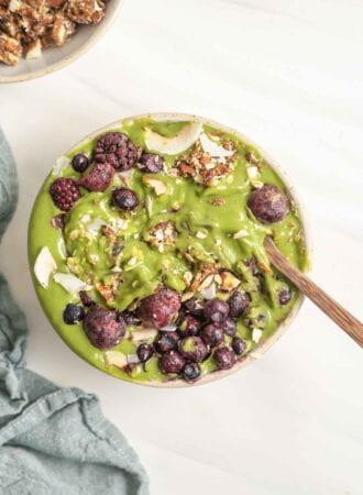 A thick green smoothie in a bowl topped with berries and nuts.