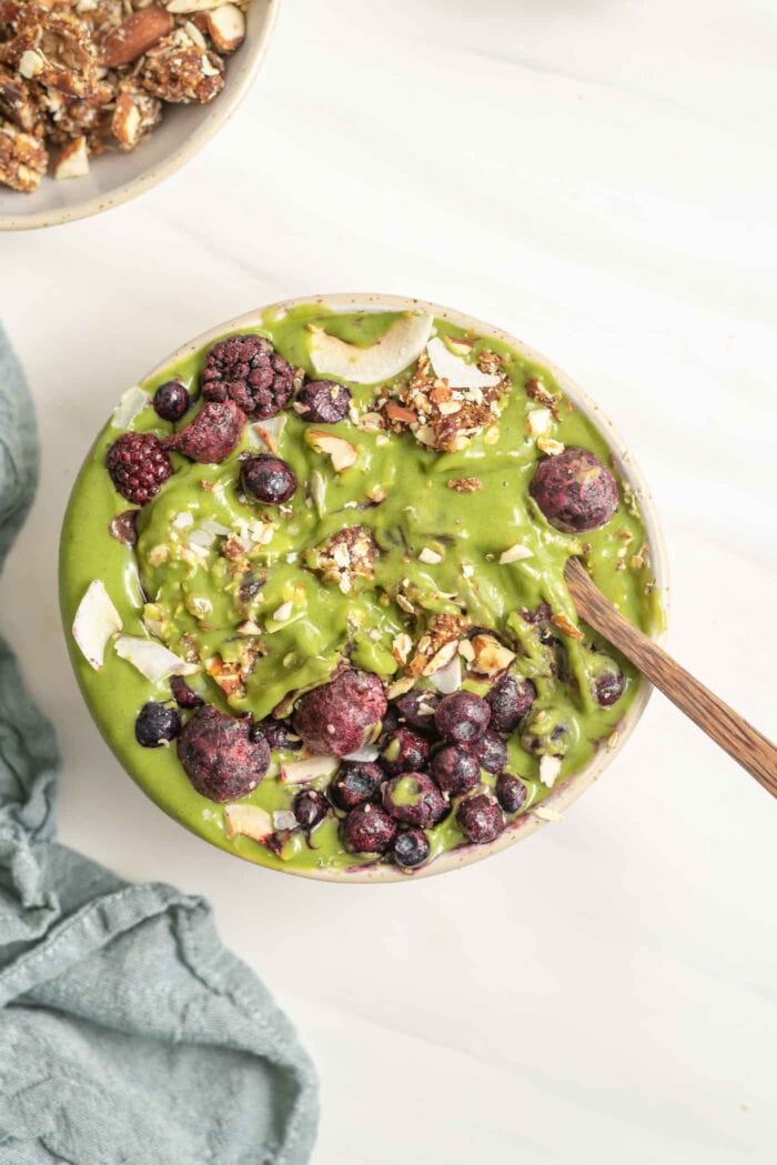 A thick green smoothie in a bowl topped with berries and nuts.