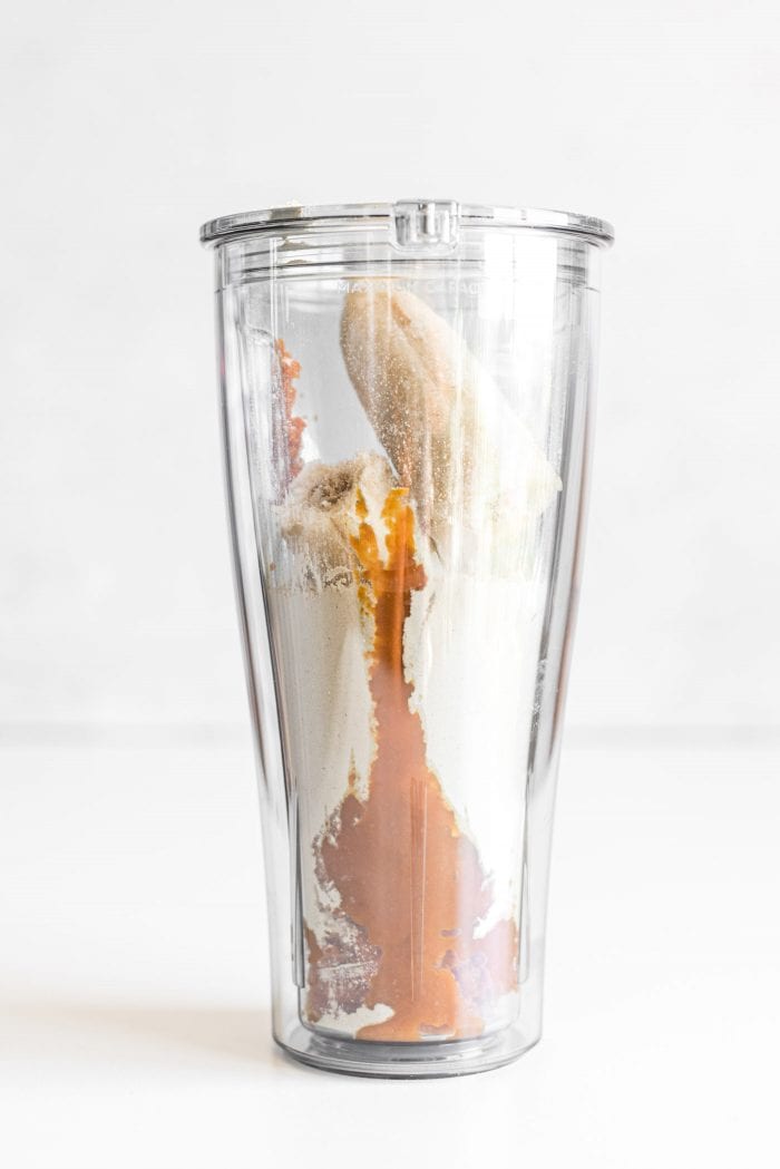 Pumpkin puree, frozen banana and vegan protein powder in a blender cup.