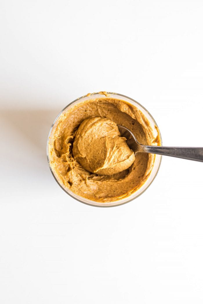 Vegan pumpkin pie protein pudding in a glass jar being scooped with a spoon.