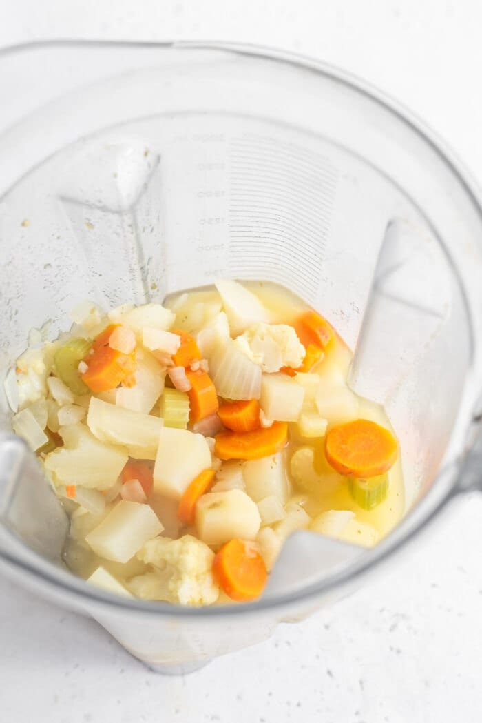 Chopped, cooked vegetables and broth in a Vitamix ready to be blended.