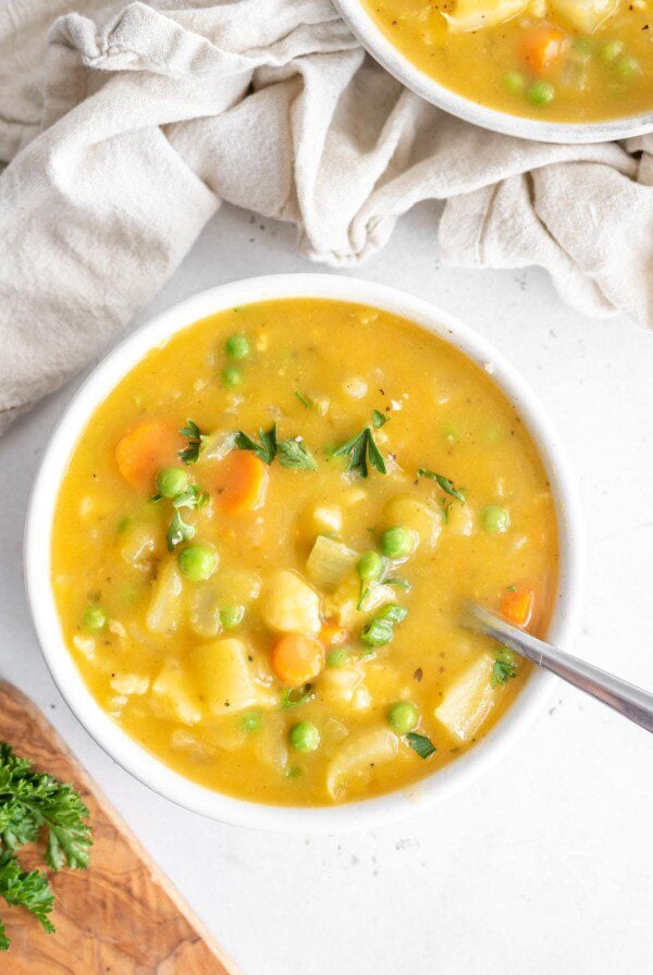 Bowl of cauliflower potato soup with peas on a white background with a beige napkin.