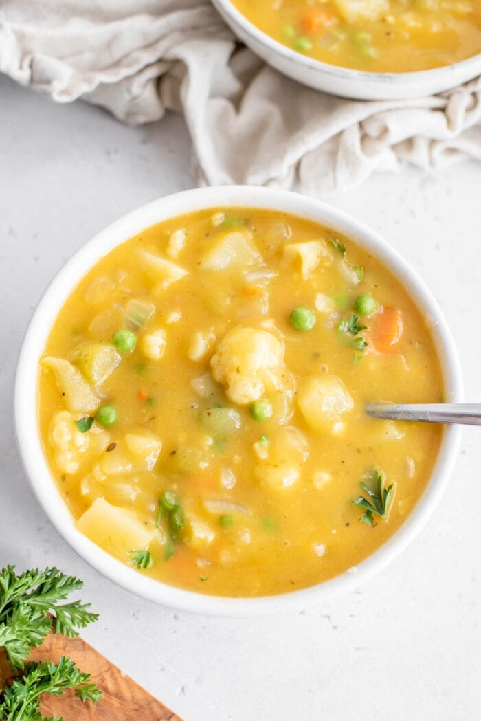 A bowl of creamy cauliflower and potato soup with green peas in it.