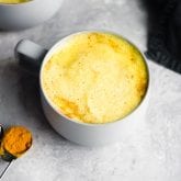 A mug of golden milk with a spoon of turmeric beside it.