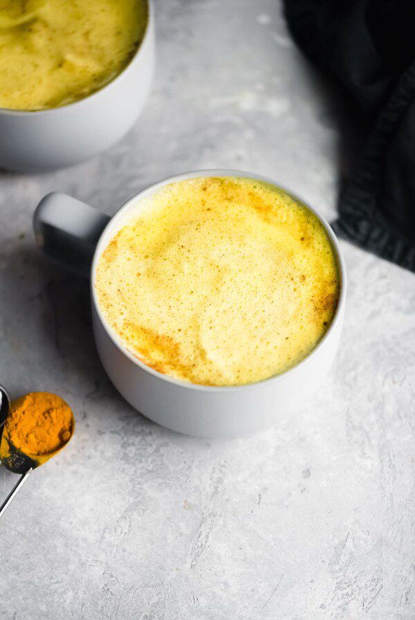 A mug of golden milk with a spoon of turmeric beside it.